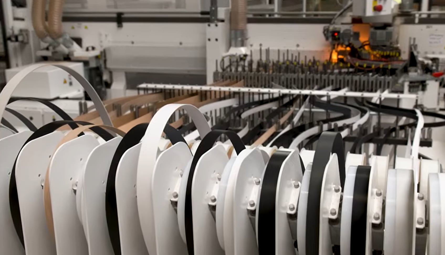 In der Fertigung werden Kantenbänder automatisiert einer Kantenanleimmaschine zugeführt. Die Anlage verarbeitet unterschiedliche Kantenmaterialien.